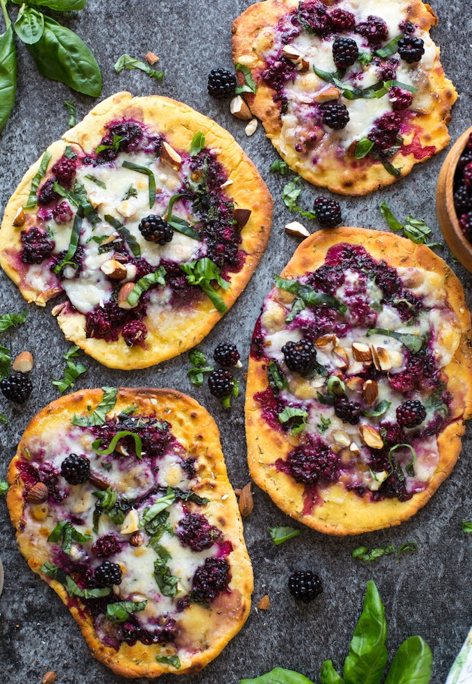 4 blackberry flatbread pizzas on a granite background topped with basil and almonds