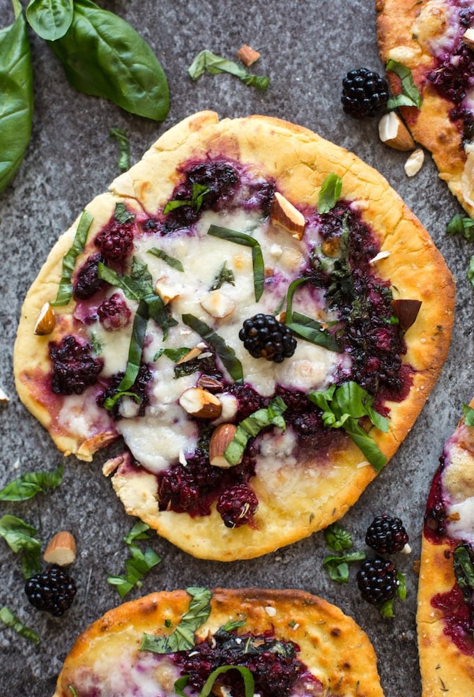 blackberry flatbread pizzas on a granite background topped with basil and almonds