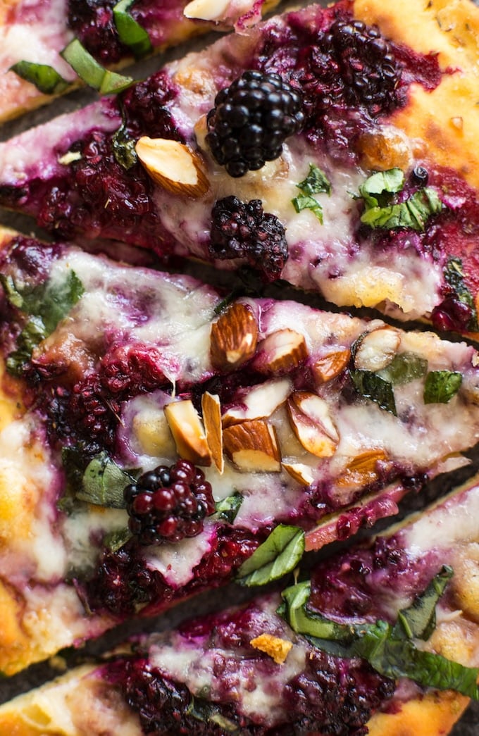 up close blackberry flatbread pizza sliced on a granite background topped with basil and almonds