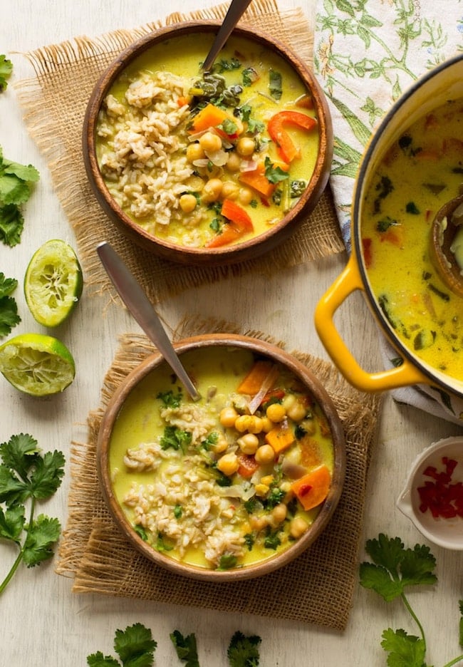  two bowls of Chickpea Lime & Coconut Soup in a wooden bowl with limes on the side