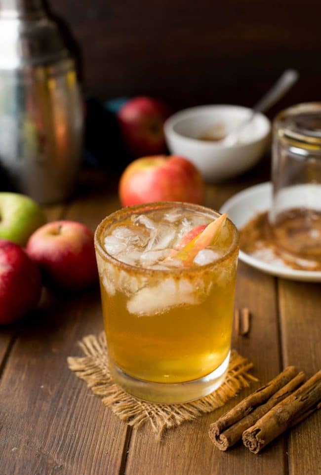 Apple Margarita in a glass surrounded by apples and cinnamon sticks