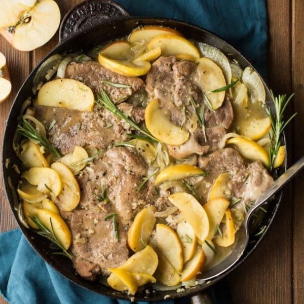 Cider Braised Pork Chops with Apple & Onions in a cast iron skillet surrounded by apples