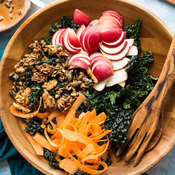 Crunchy kale apple salad in a salad bowl with salad tongs
