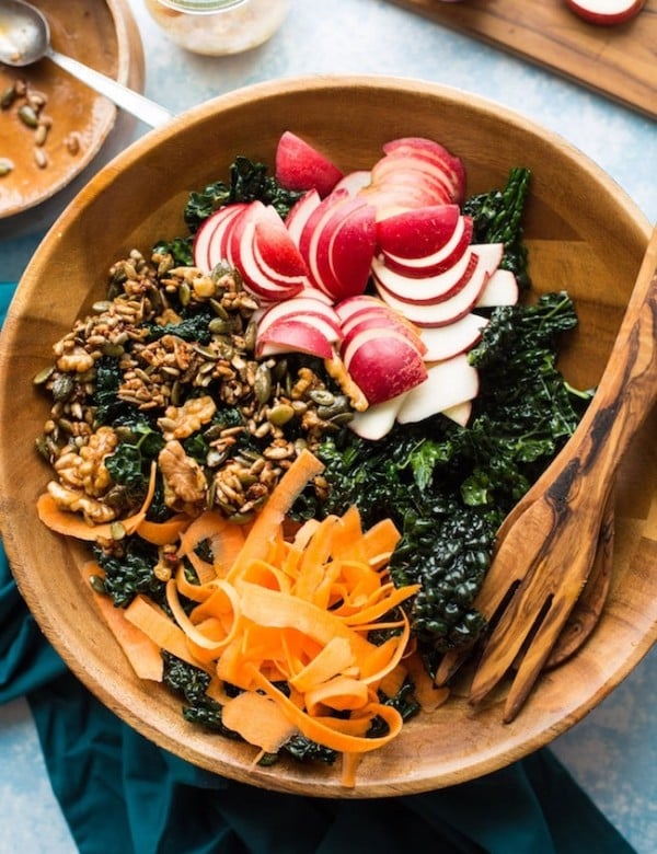 Crunchy kale apple salad in a salad bowl with salad tongs