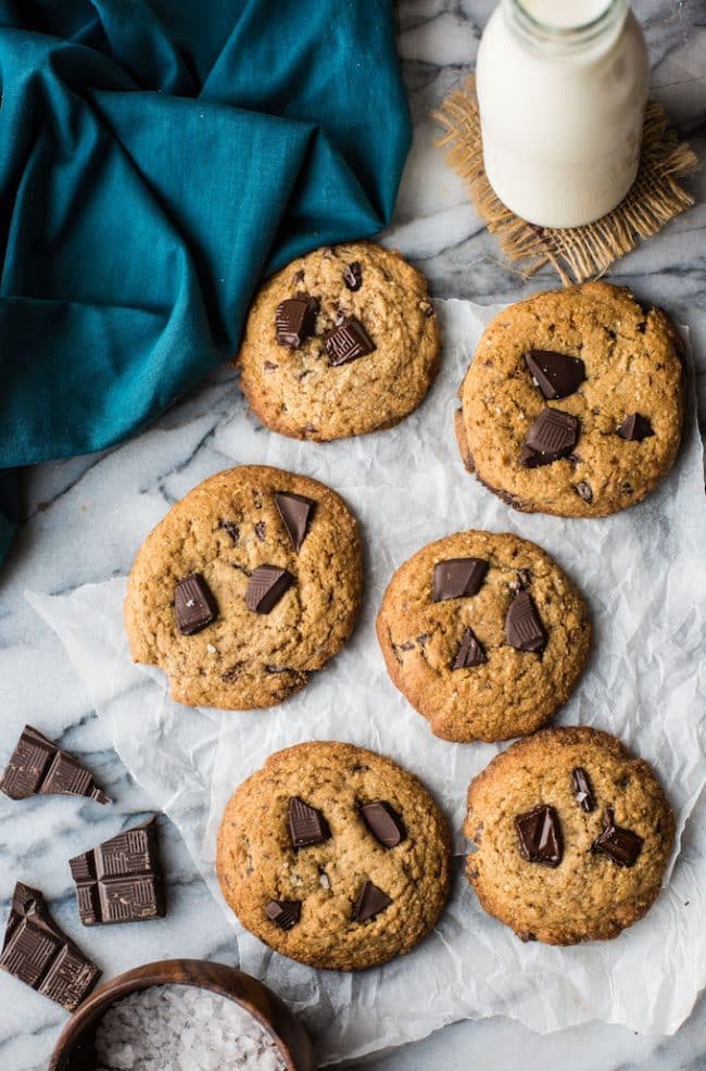 Soft and chewy Paleo Chocolate Chip Cookies on a piece of parchment paper with chocolate chunks and a glass of milk