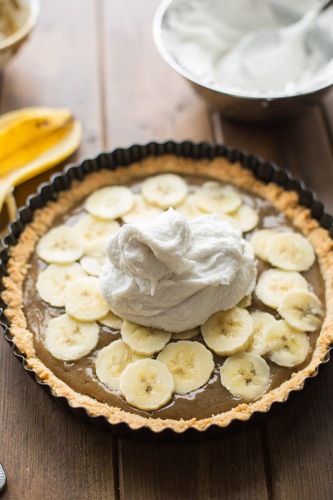 Rich and decedent Vegan Banoffee Pie - a simple, almond flour crust topped with silky caramel, banana, coconut whipped cream and a drizzle of chocolate | Gluten Free + Paleo  | Spreading coconut cream over the top of the pie