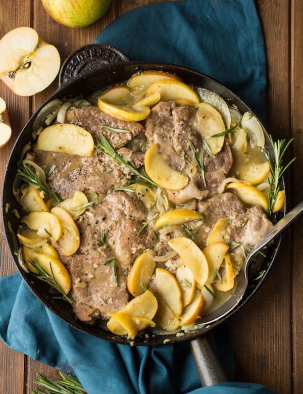 cider braised pork chops topped with fresh rosemary in a cast iron pan