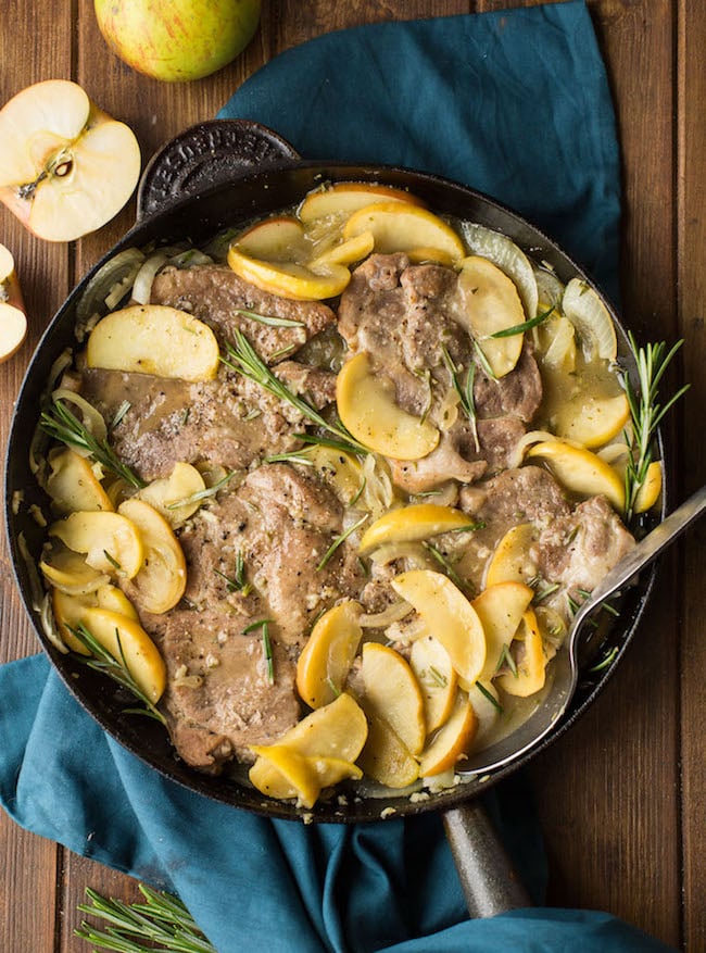 cider braised pork chops topped with fresh rosemary in a cast iron pan