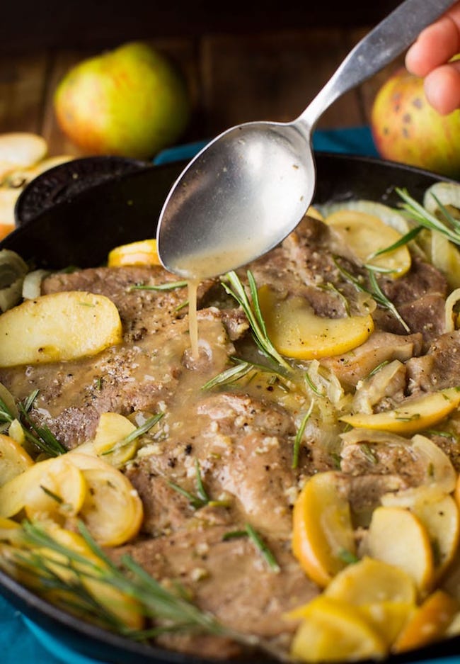 spoon spooning over juices on cider braised pork chops topped with fresh rosemary in a cast iron pan