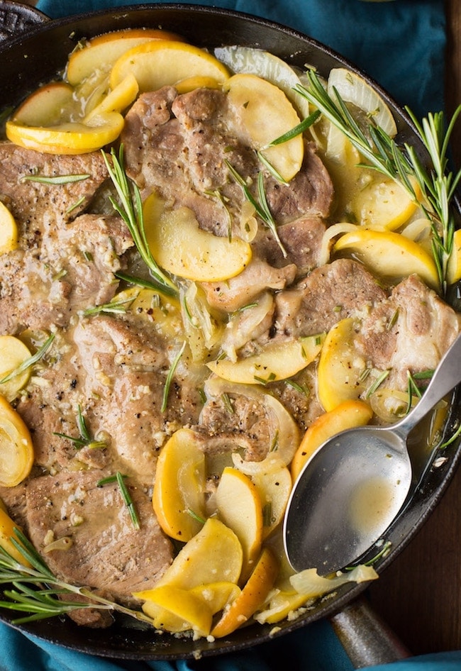 cider braised pork chops topped with fresh rosemary in a cast iron pan