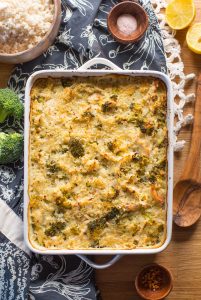 Chicken & Broccoli Cauliflower Rice Casserole in a rectangular baking dish on a blue bad white apron