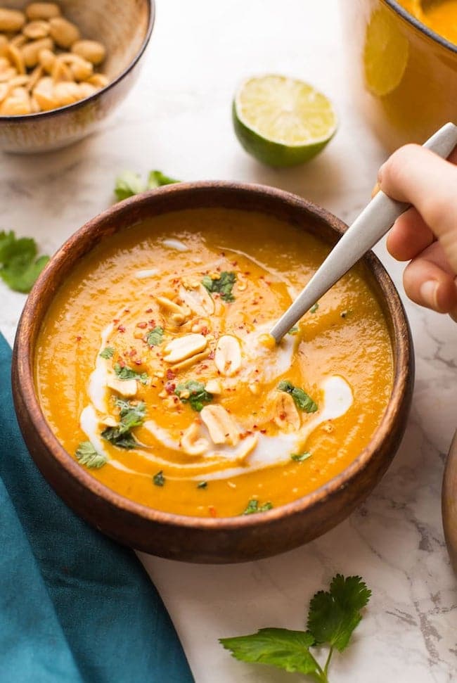 Peanut Carrot & Sweet Potato Soup in a bowl with a hand holding a spoon