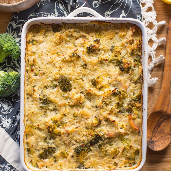 chicken broccoli cauliflower casserole on a wooden table with broccoli and spoon next to it