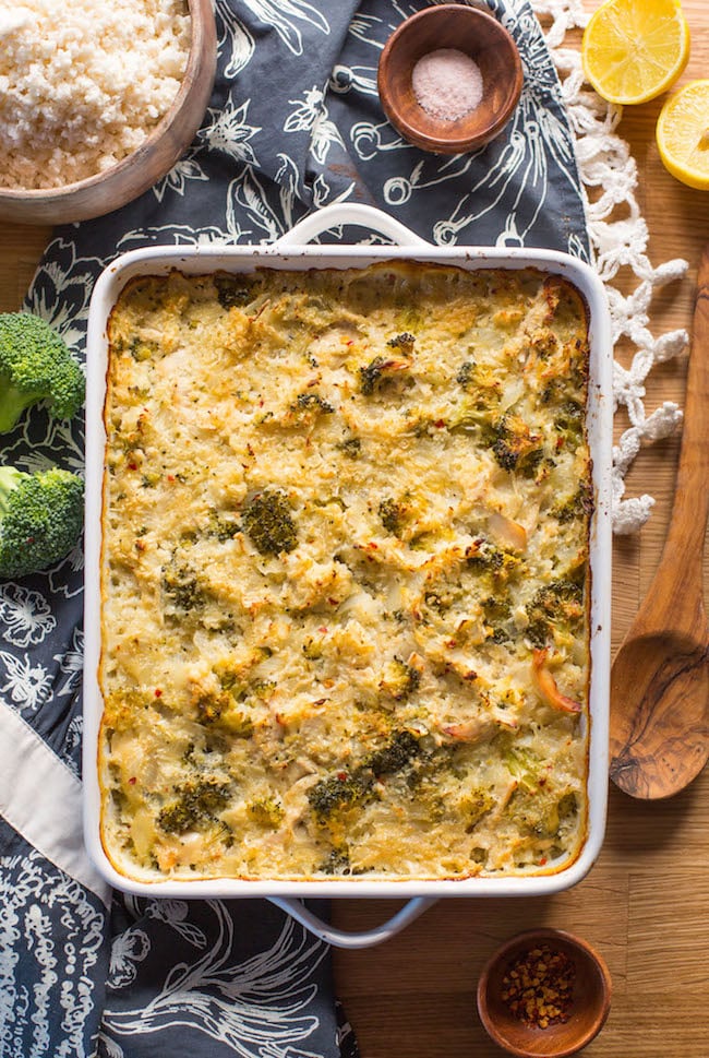 chicken broccoli cauliflower casserole on a wooden table with broccoli and spoon next to it