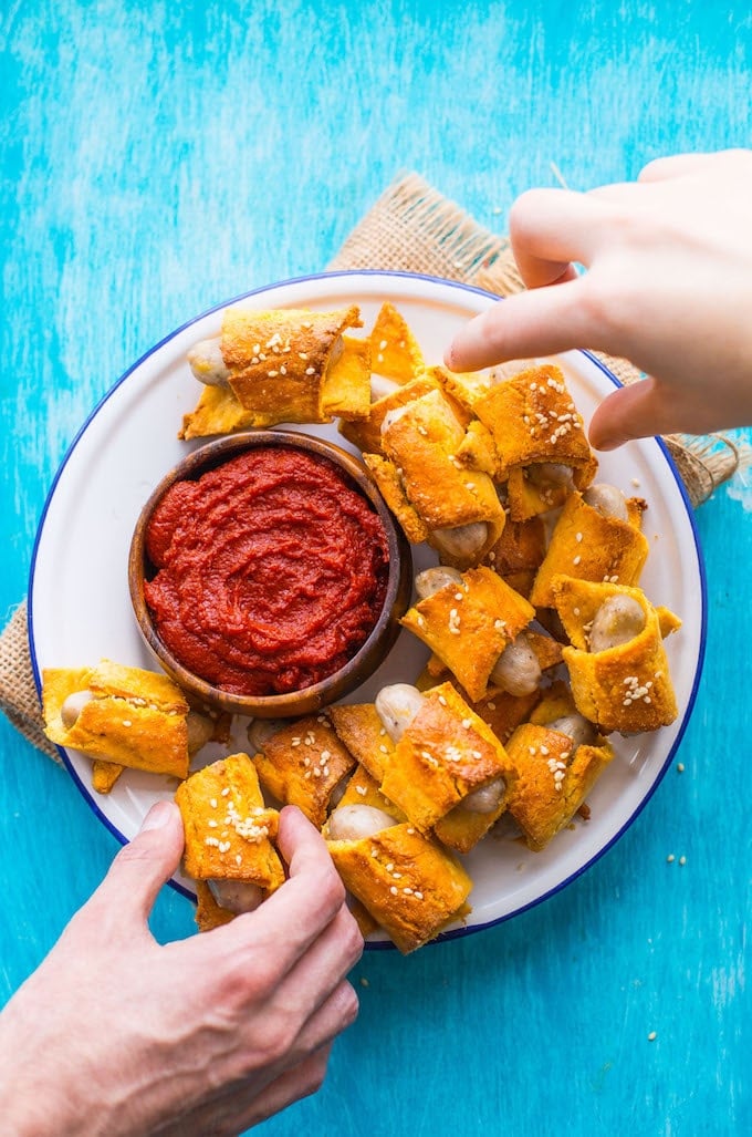 Paleo Pigs in a Blanket on a plate with ketchup and hands reaching towards the plate