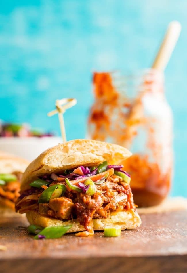 BBQ Jackfruit Pulled 'Pork' Sandwich on a cutting board with BBQ sauce in the background