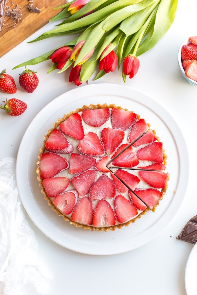 Strawberry Vanilla Vegan Cheesecake - A thick and creamy cashew vanilla cream topped with sliced strawberries over a layer of melted chocolate and a naturally sweetened date & hazelnut crust | #Paleo + #Raw + #GlutenFree