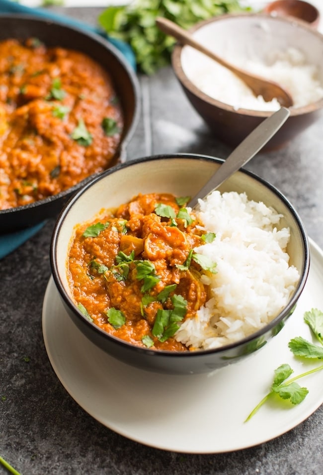 Tomato & Turmeric Shrimp Curry served in a black bowl with a side of white rice