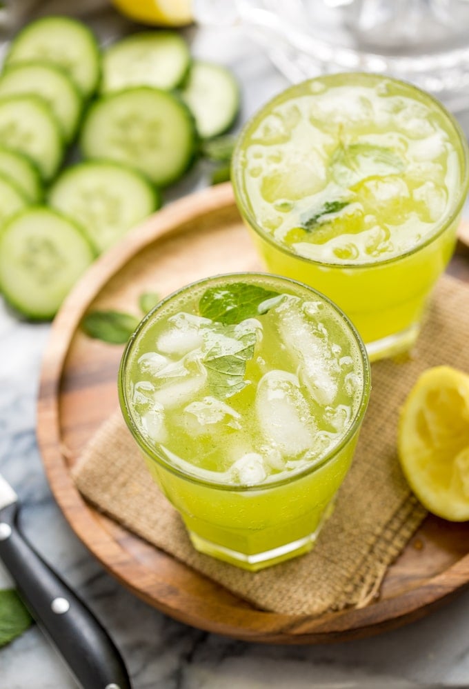 Minty Cucumber Lemonade with ice surrounded by ucucumbers