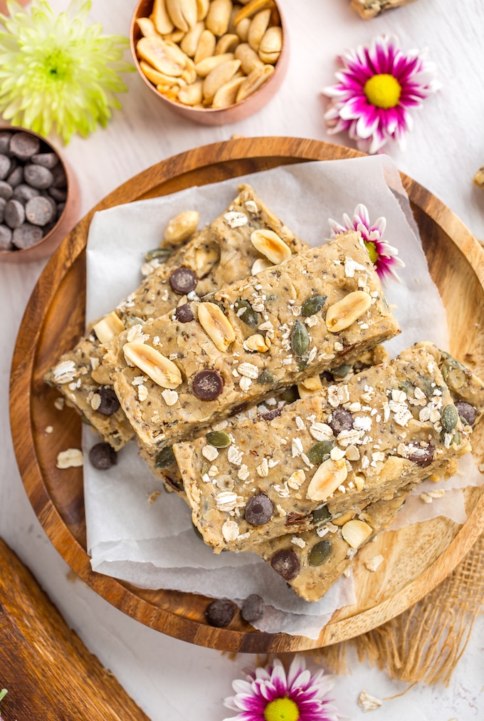 Peanut Butter No Bake Granola Bars sitting on a plate with a salted peanuts, chocolate chips and pink flowers surrounding 