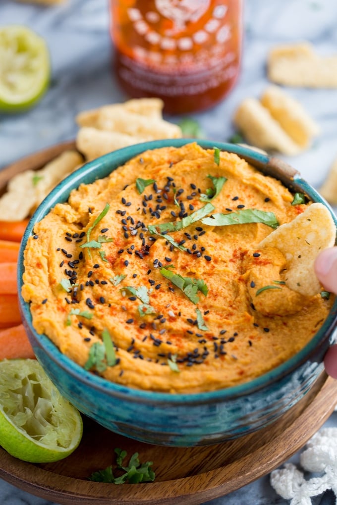 Sriracha Lime Hummus topped with black sesame seeds, fresh cilantro and a chip