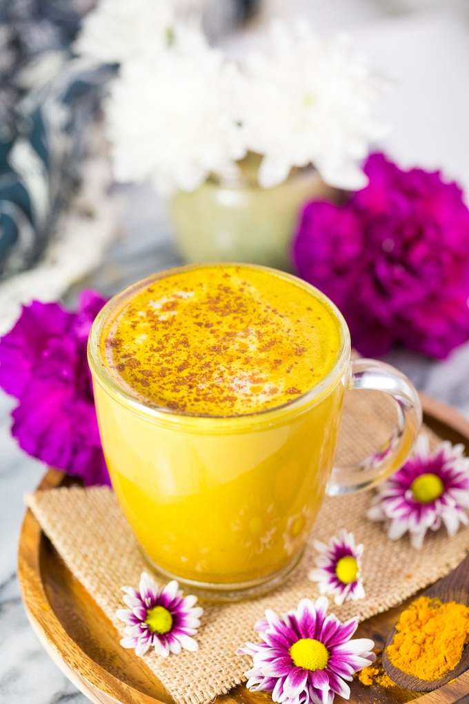 Golden Turmeric Latte with cinnamon sprinkled over the top on a plate surrounded by white and pink flowers