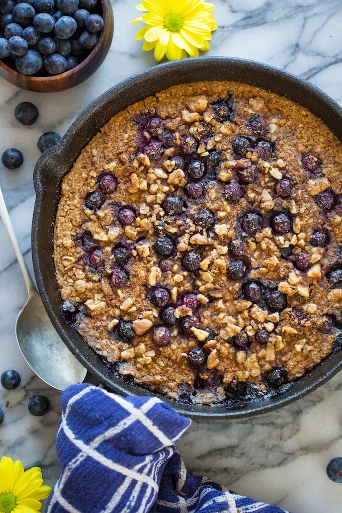 Blueberry Oatmeal Bake in a cast iron skillet surrounded but flowers and blueberries
