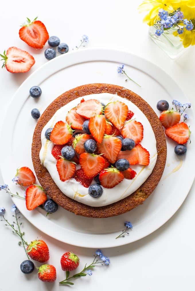 a single layer coconut flour cake topped with whipped coconut cream and berries on a plate with little flowers