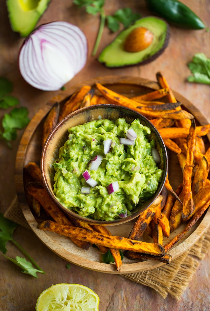 Homemade Guacamole Recipe on a plate with sweet potato fries on topped with chopped onions