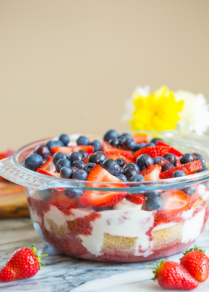 Summer Berry Coconut paleo Trifle in a bowl and topped with berries with flowers in the background