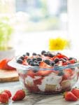 Summer Berry Coconut PAleo Trifle in a bowl and topped with berries with flowers in the background