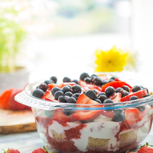 Summer Berry Coconut PAleo Trifle in a bowl and topped with berries with flowers in the background