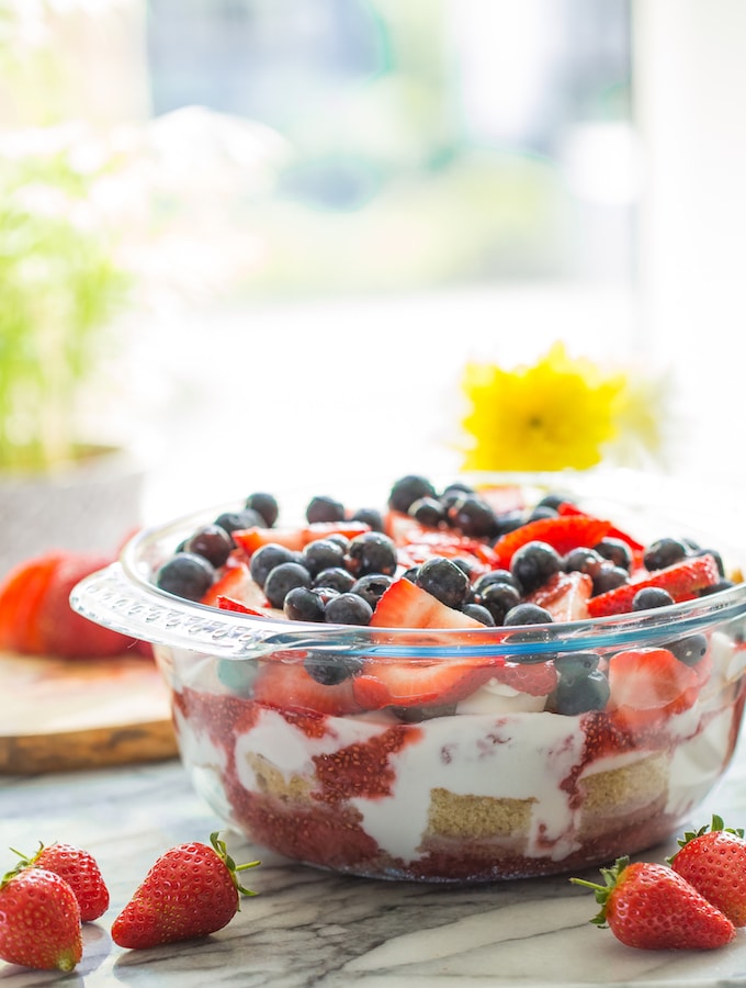 Summer Berry Coconut paleo Trifle in a bowl and topped with berries with flowers in the background