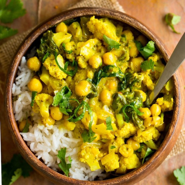 Yellow Cauliflower Chickpea Curry served over a bed of rice in a wooden bowl with a spoon