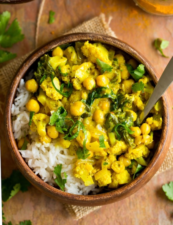 Yellow Cauliflower Chickpea Curry served over a bed of rice in a wooden bowl with a spoon