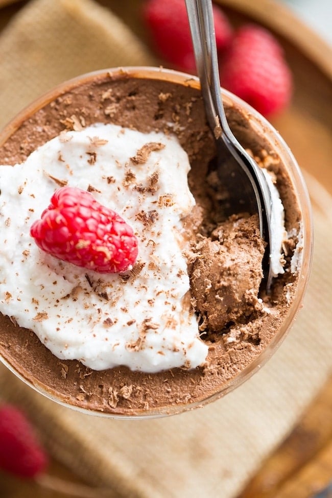 Aquafaba Chocolate Mousse up close with spoonfuls of mousse & topped with coconut whipped cream and a raspberry