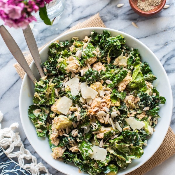 Salmon Kale Caesar Salad in a bowl with serving forks and flowers on the side