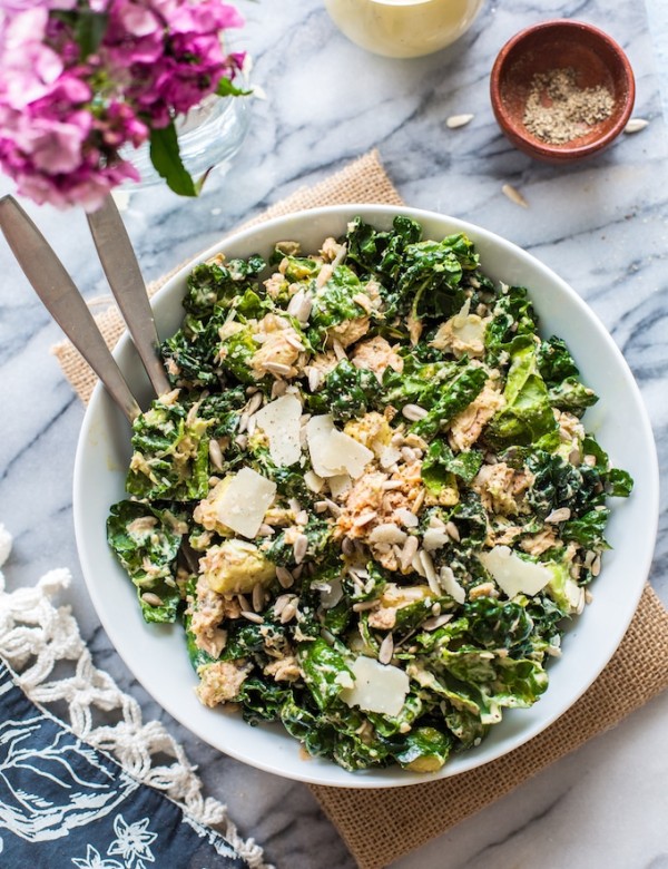 Salmon Kale Caesar Salad in a bowl with serving forks and flowers on the side