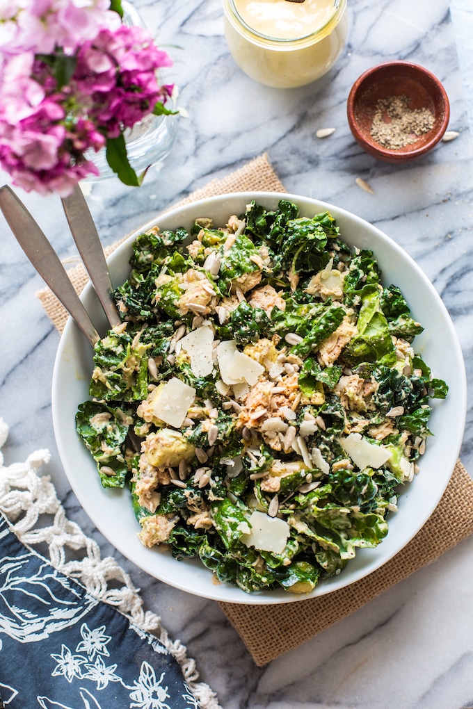 Salmon Kale Caesar Salad in a bowl with serving forks and flowers on the side