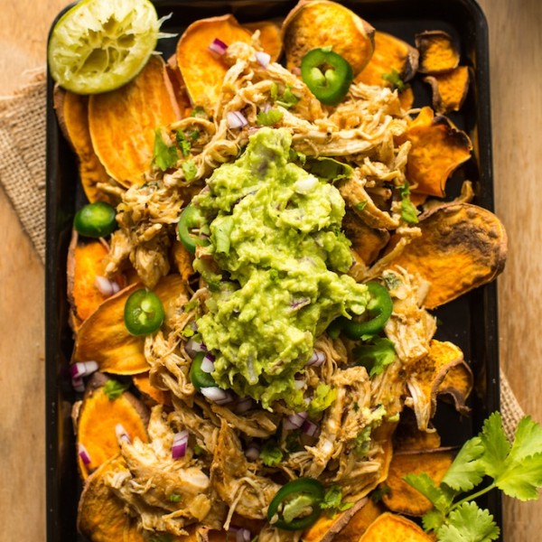 Sweet Potato Nachos on a baking sheet topped with chicken carnitas, guacamole and cilantro