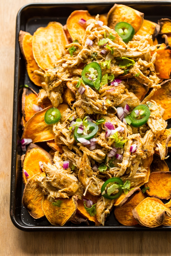 sheet potato nachos on a baking sheet topped with carnitas, chopped red onion and jalapeno