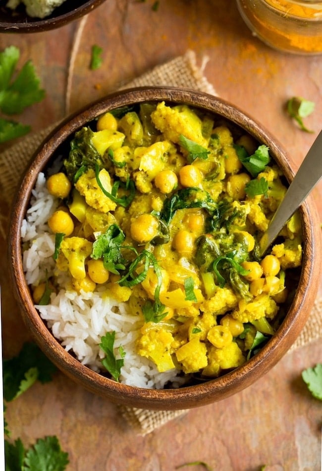 Yellow Cauliflower Chickpea Curry served over a bed of rice in a wooden bowl with a spoon