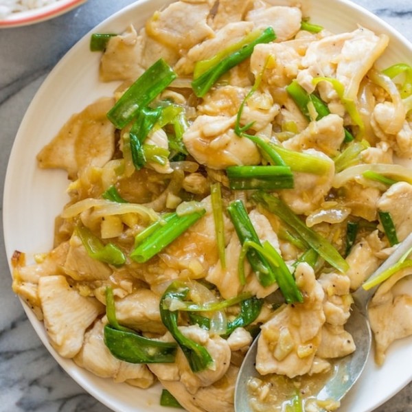 Garlic Ginger and Spring Onion Chicken on a serving plate with a spoon on a marble counter top