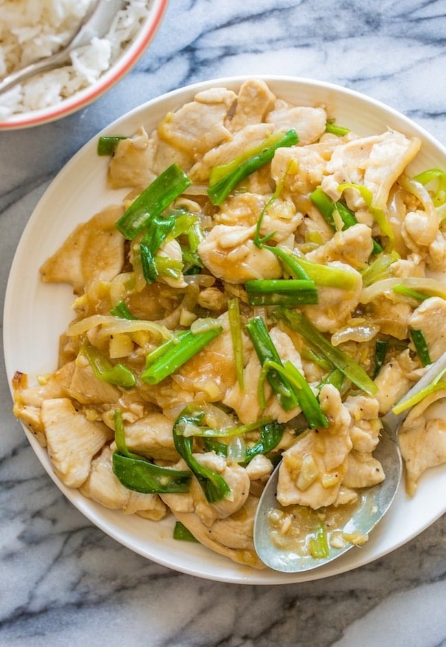 Garlic Ginger and Spring Onion Chicken on a serving plate with a spoon on a marble counter top