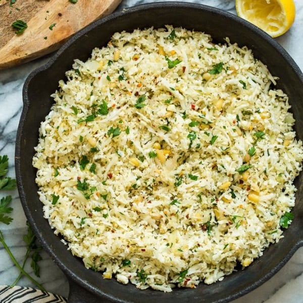 Mediterranean Cauliflower Rice in a cast iron skillet on a marble surface with lemon and parsley surrounding