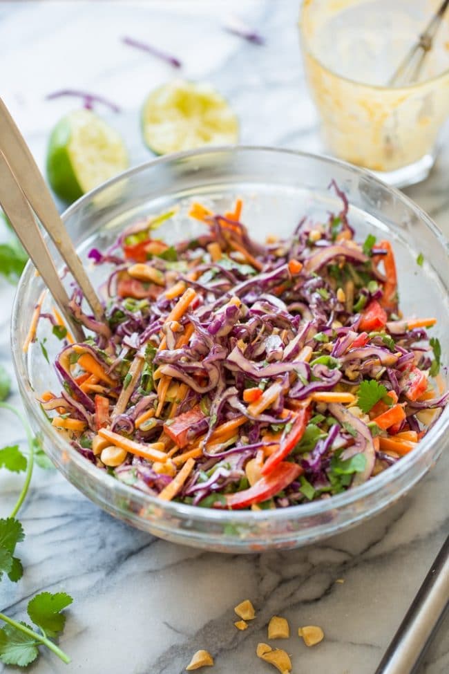 Thai Peanut Coleslaw on a marble counter surrounded by limes and cilantro