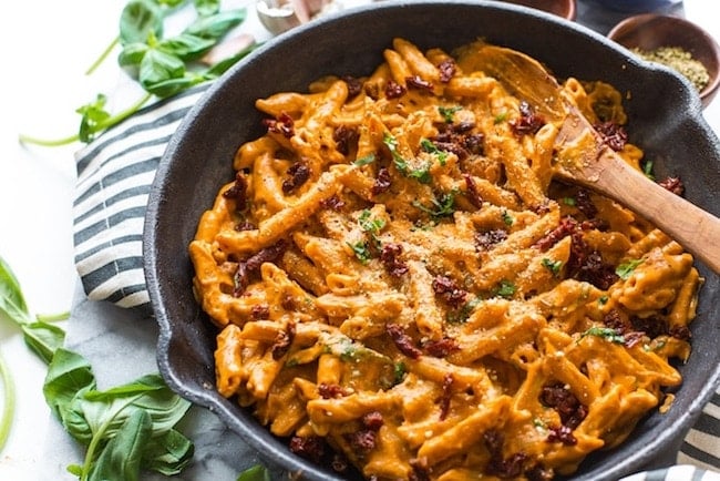 Vegan Sun Dried Tomato Alfredo in a cast iron skillet on top of a black and white stripped kitchen towel with fresh basil