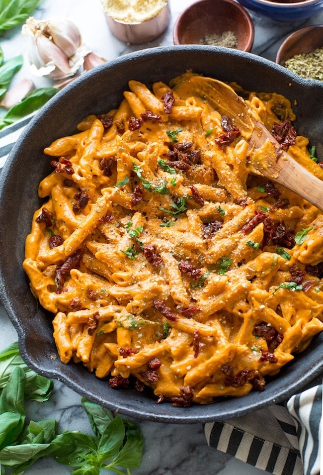 Vegan Sun Dried Tomato Alfredo in a cast iron skillet with a wooden spoon and topped with fresh basil