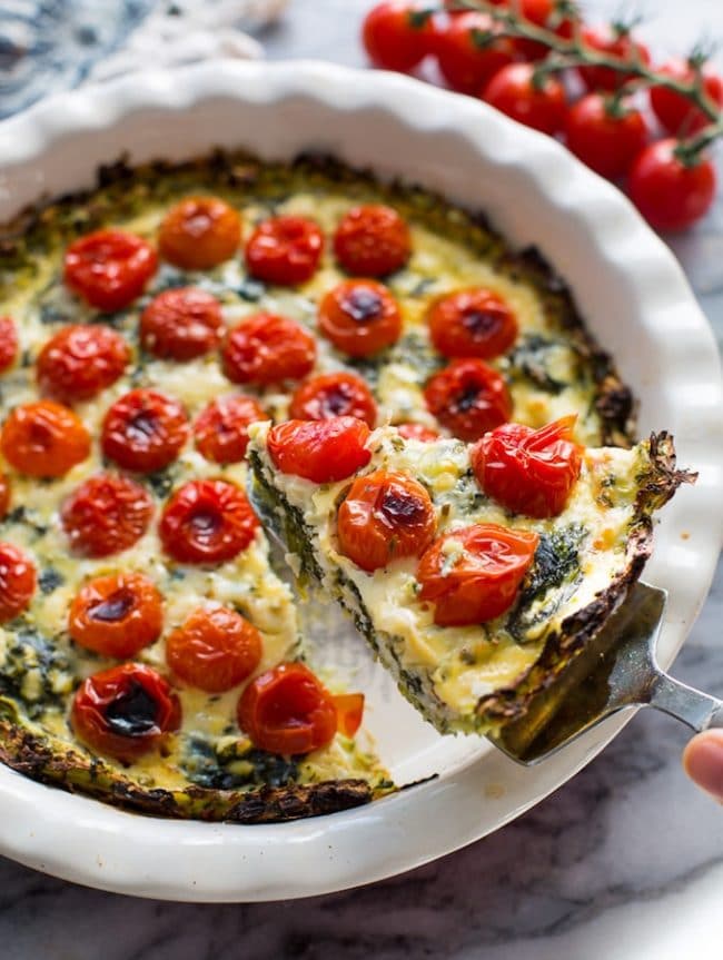 Zucchini Crust Tomato Spinach Feta Pie in a pie plate with a slice lifted up on a spatula