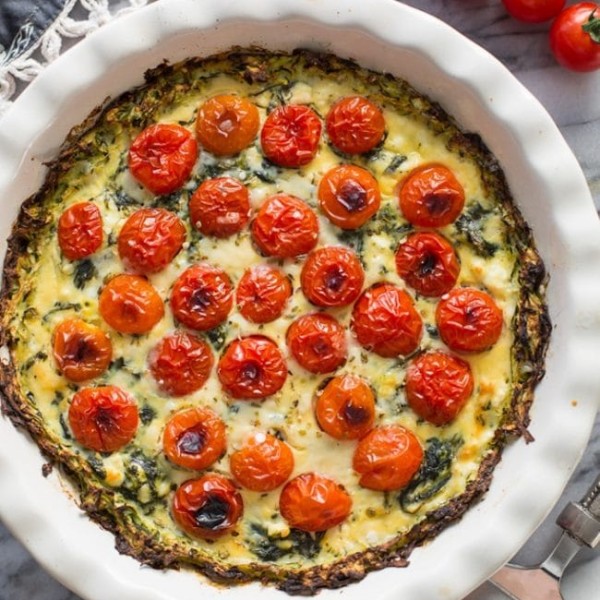 Zucchini Crust Tomato Spinach Feta Quiche in a pie plate on a marble counter top